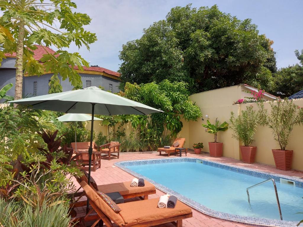Bijilo的住宿－Bougainvillea House，一个带遮阳伞和椅子及桌子的游泳池