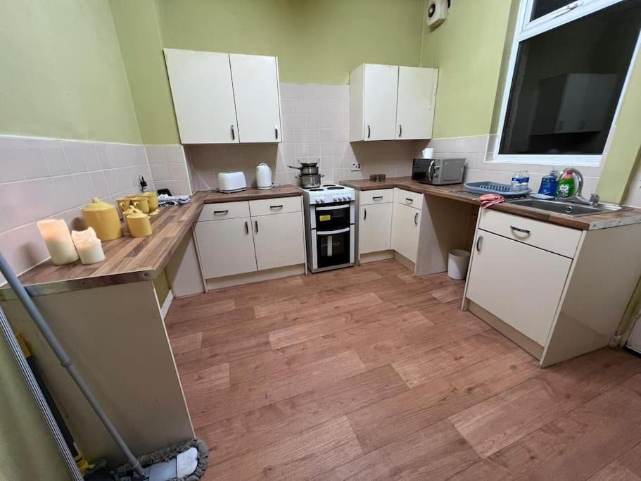 a kitchen with white cabinets and a wooden floor at Cosy 2 Bed House in Rochdale in Rochdale