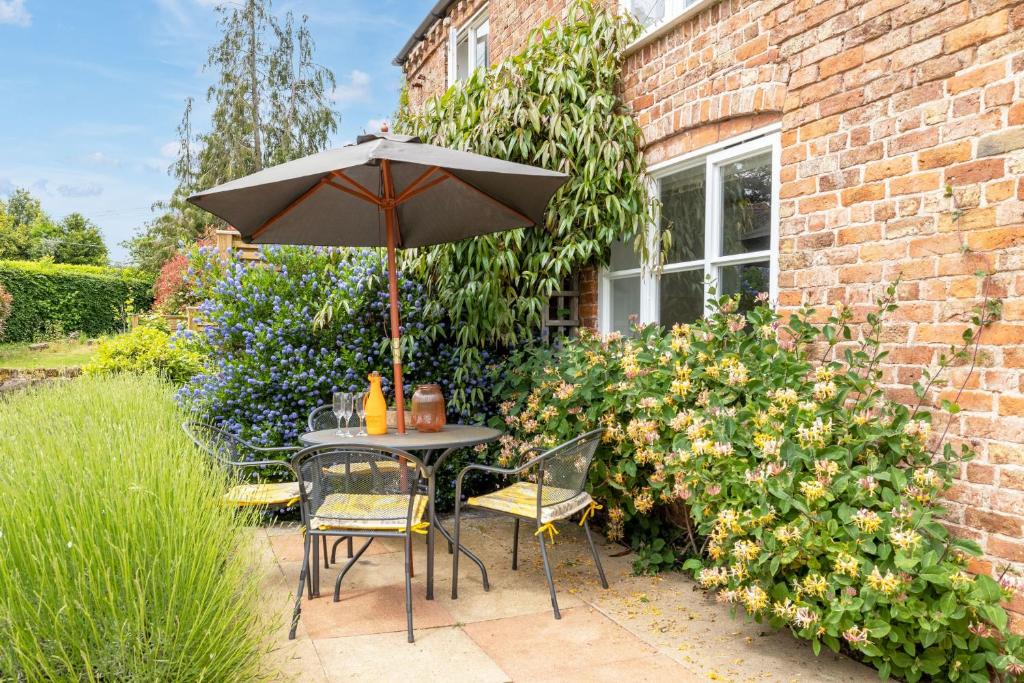 a table and chairs with an umbrella in a garden at Hop Pickers Cottage in Little Marcle