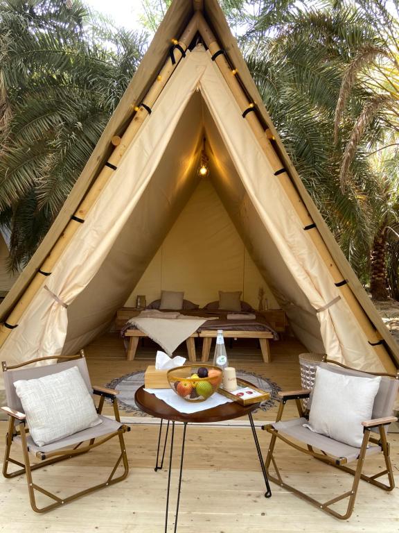 a tent with chairs and a table in front of it at Husaak Glamping in AlUla