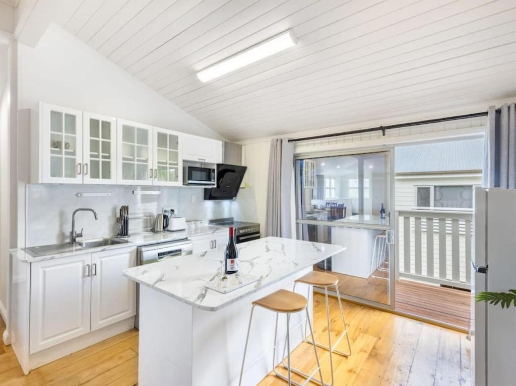 una cocina con armarios blancos y una barra con taburetes en Family friendly cozy 4BR house at Annerley, en Brisbane
