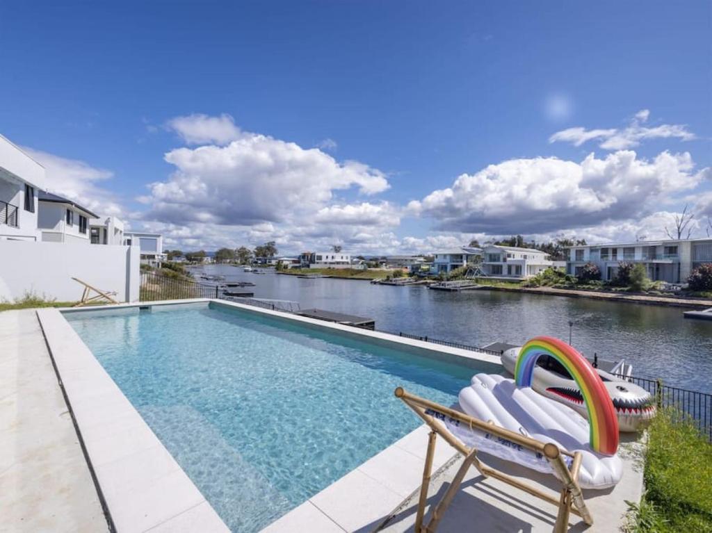 a swimming pool with a chaise lounge next to a river at Stunning waterfront family home with pontoon newly in Gold Coast