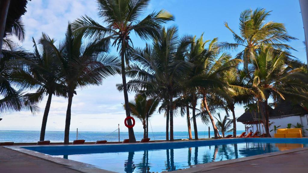 a swimming pool with palm trees next to the ocean at Sky & Sand Zanzibar Beach Resort in Pwani Mchangani