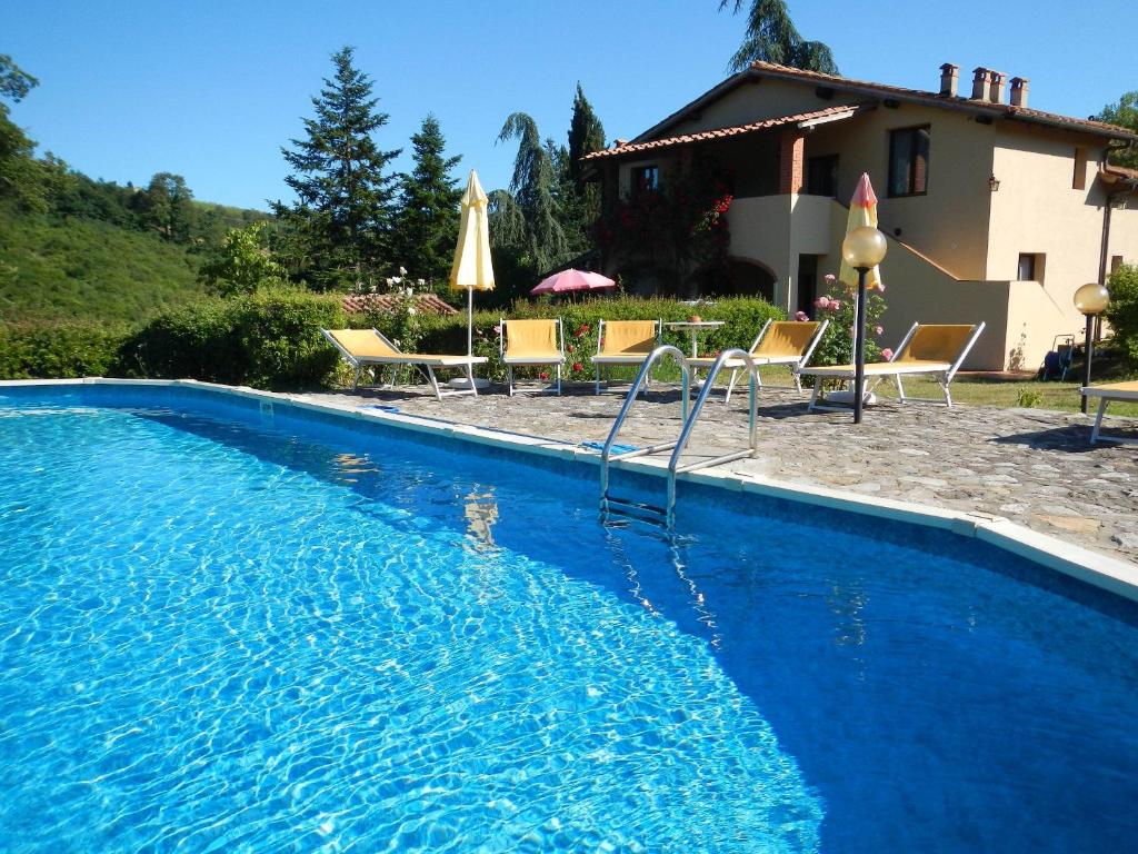 a blue swimming pool with chairs and a house at Villa Buonasera Agriturismo in Greve in Chianti