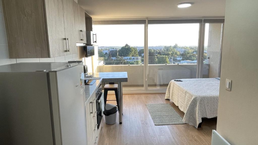 a kitchen with a refrigerator and a table and a bed at Depto central, parking, moderno in Chillán