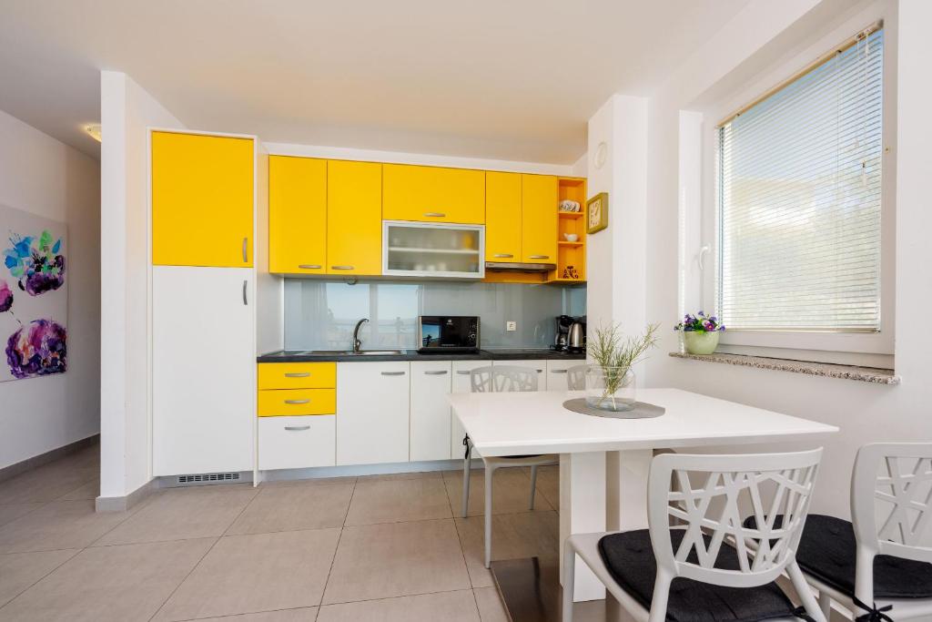 a kitchen with yellow cabinets and a white table and chairs at Apartments Petak Novi in Dramalj