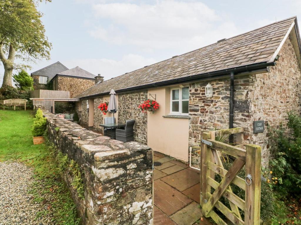 a stone cottage with a stone wall and a fence at Cosy Cottage in Lifton