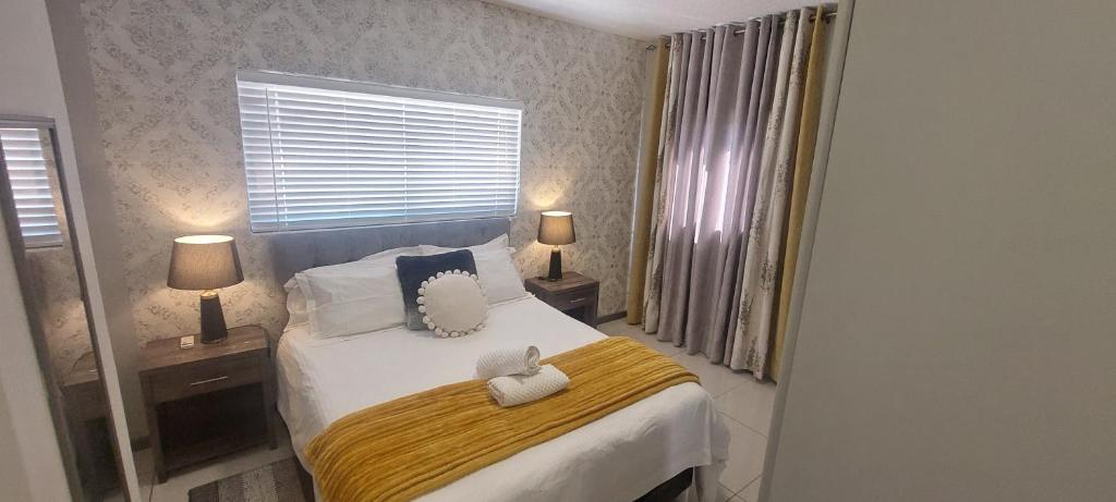 a bedroom with a bed with a yellow blanket and two lamps at Bee's Central Hideout in Windhoek