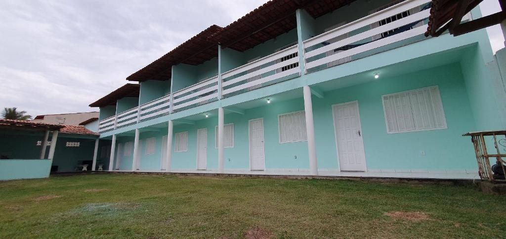 a blue building with white doors and a grass yard at Vila Mar Flats - 1 Dorm - Guriri - 800m da Praia in São Mateus