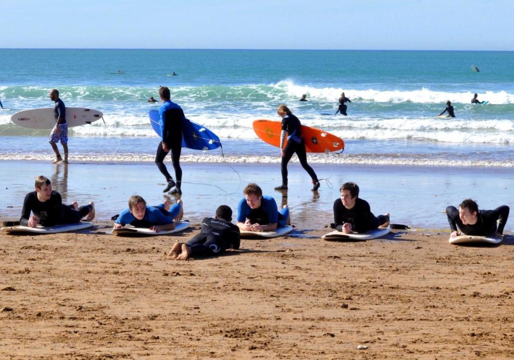 Surf Lessons Experience with Hassi في أغادير: مجموعة من الناس يجلسون على الشاطئ مع ألواح ركوب الأمواج