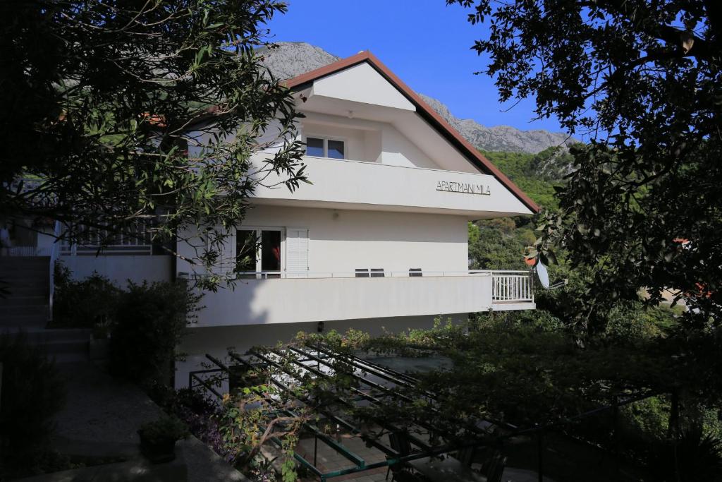 ein weißes Haus mit einer Frau auf einem Balkon in der Unterkunft Apartments by the sea Zivogosce - Mala Duba, Makarska - 21781 in Živogošće