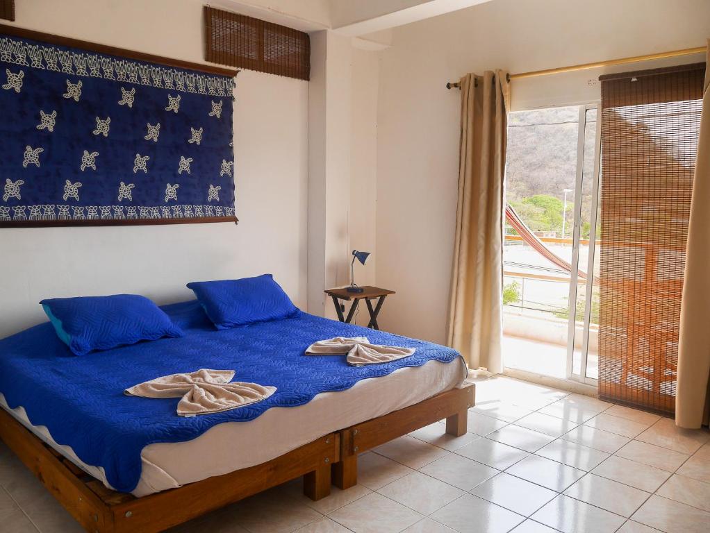 Schlafzimmer mit einem Bett mit blauer Bettwäsche und einem Fenster in der Unterkunft Sierraventura Hostel in Taganga