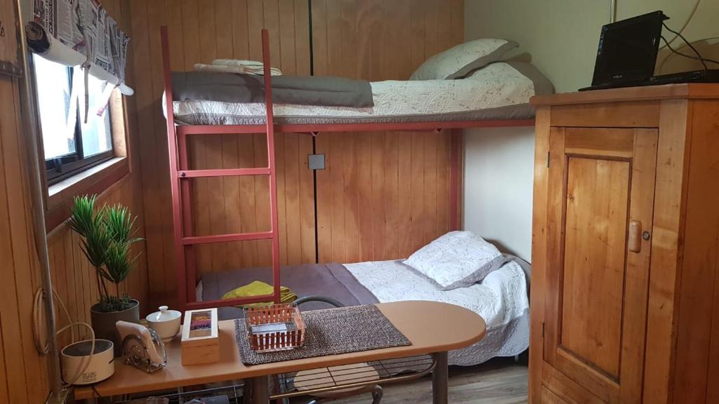 a room with bunk beds and a desk and a table at CABAÑA EL BUHO - ESMERALDA in Puerto Natales