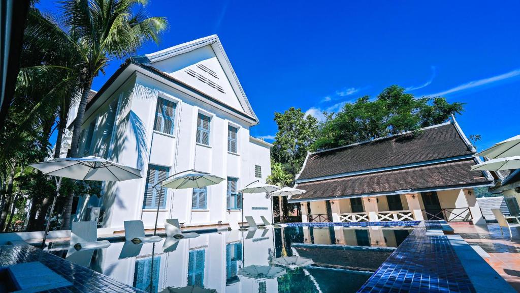 a swimming pool in front of a building with umbrellas at JingLand Hotel Luangprabang in Luang Prabang