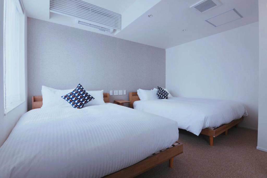 two beds in a room with white sheets and pillows at KABIN Minamiza in Kyoto