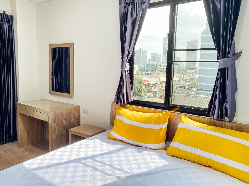 GP House Bangkok - Sukhumvit Onnut BTS Skytrain في بانكوك: غرفة نوم بسرير ومخدات صفراء ونافذة