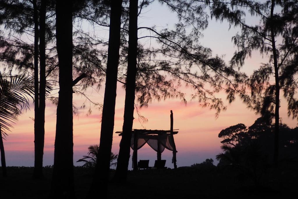 einen Sonnenuntergang durch die Bäume mit einem Tisch und einem Kreuz darauf in der Unterkunft The Moken Eco Village - SHA plus in Ko Phra Thong