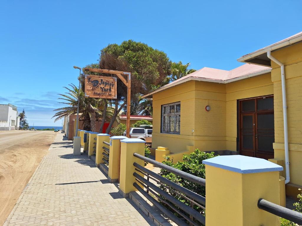 a yellow building with a fence next to a street at Japie's Yard Wanderer's Inn in Swakopmund