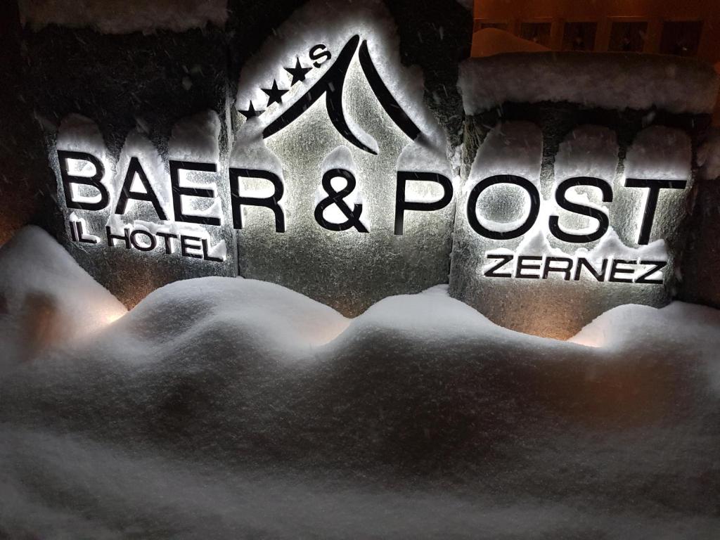 ein Schild für eine Bar und ein Hotel im Schnee posten in der Unterkunft Hotel Baer & Post Zernez in Zernez