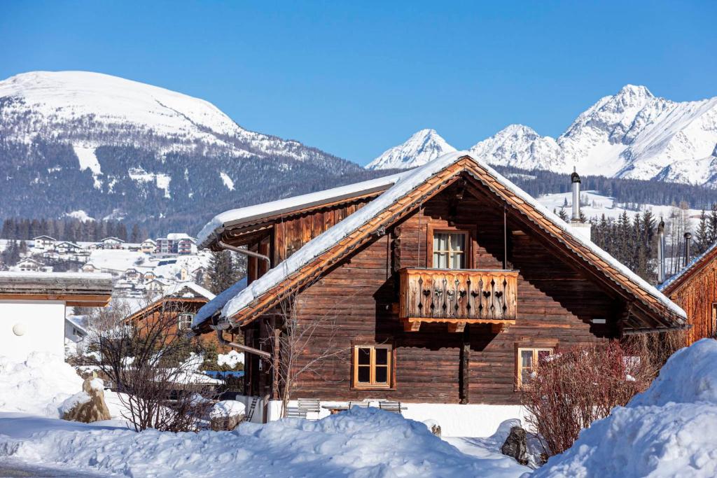 a log cabin in the snow with snow covered mountains at Alm Chalet Grosseck in Mariapfarr