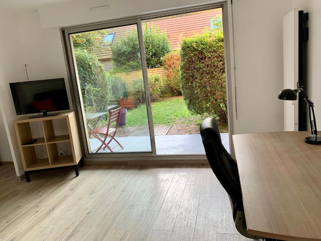 un bureau avec une table, une télévision et une porte coulissante en verre dans l'établissement Studio indépendant + jardin, à La Frette-sur-Seine