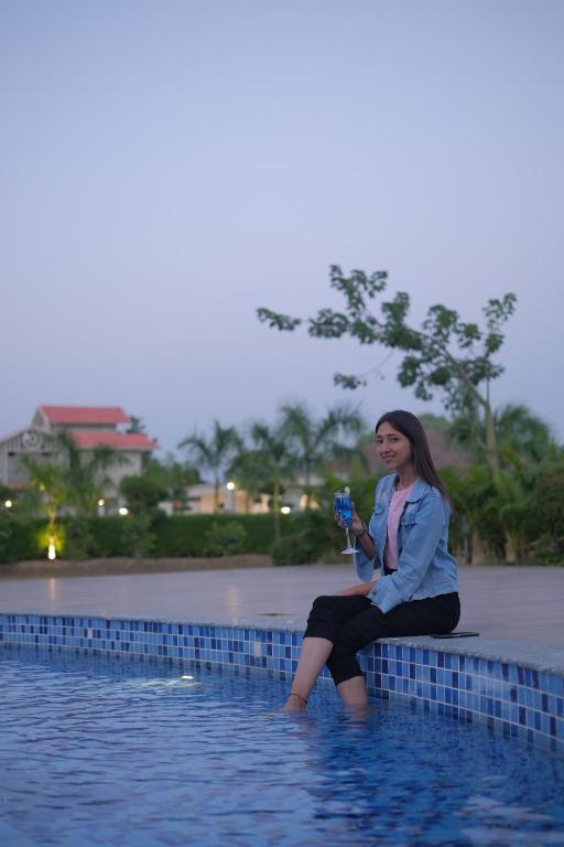 una mujer sentada en una pared en el agua en Beyond The Corbett Tales Resort and Spa en Rāmnagar
