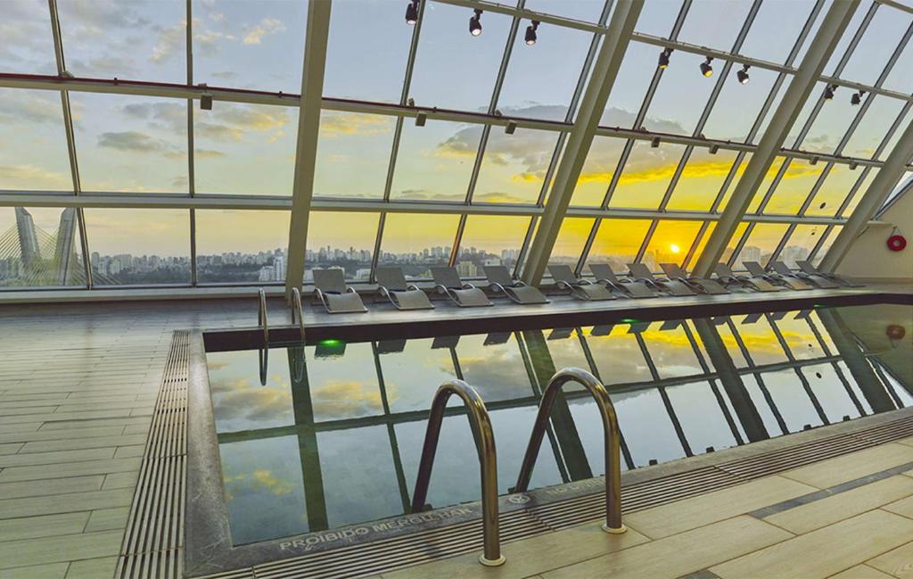 a pool in a building with chairs and a large window at Hilton Sao Paulo Morumbi in Sao Paulo