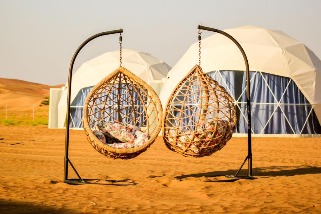 deux paniers suspendus à des poteaux devant les tentes dans l'établissement Golden Desert Camp, à Al Wāşil