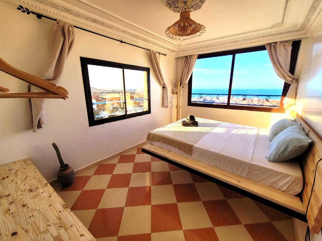 1 dormitorio con 1 cama con ventanas y suelo a cuadros en Good Wave Surf House en Tamraght Ou Fella