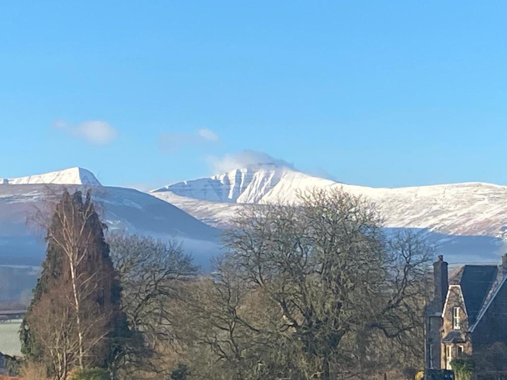 a snow covered mountain in the distance with a church and a house at Mountain Suite, Stunning Views, Brecon Beacons in Llanhamlach
