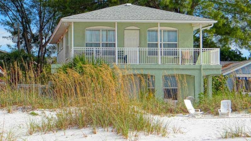 a green house with a balcony on the beach at North Shore Duplex #54588 Duplex in Anna Maria