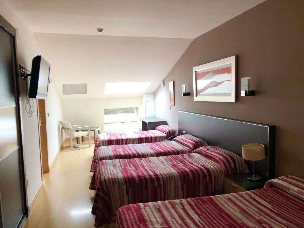 Habitación de hotel con 3 camas con sábanas a rayas en Hotel Villa de Cacabelos, en Cacabelos