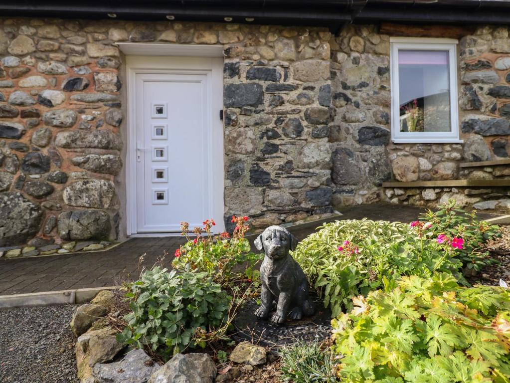a statue of a dog sitting in front of a stone house at Bryn Eglwys Barn in Tywyn