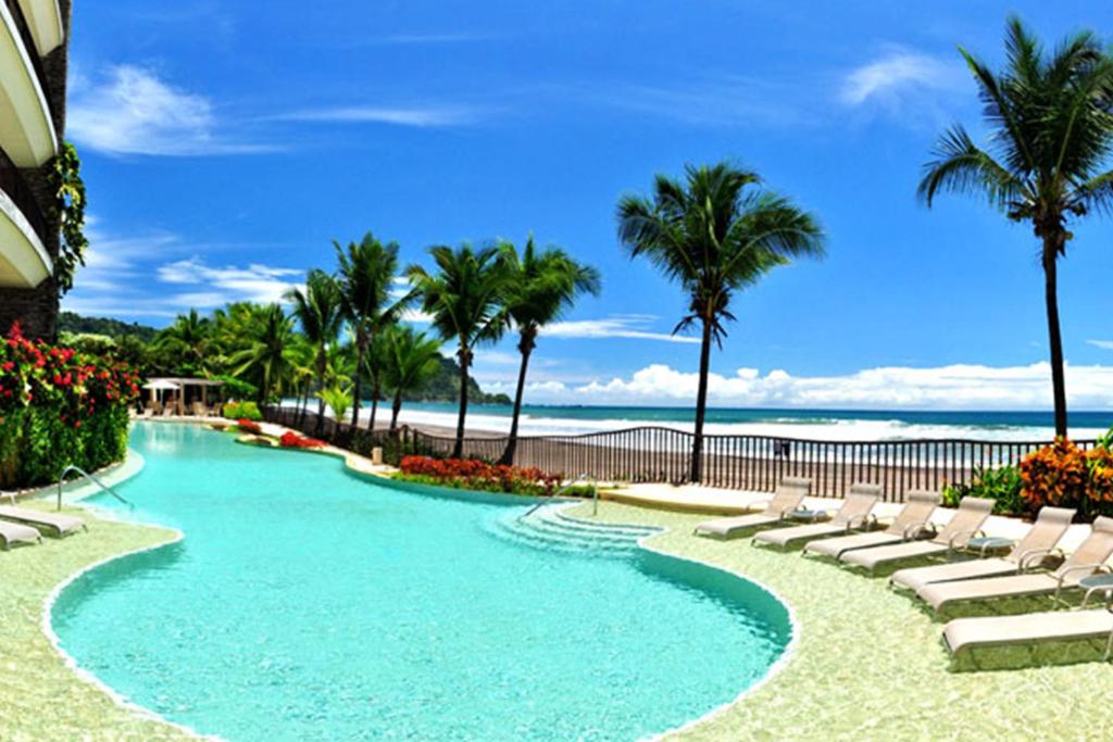 una piscina con tumbonas y la playa en SecretJaco - Luxury Beach Front Penthouse with Pool & Jacuzzi, en Jacó