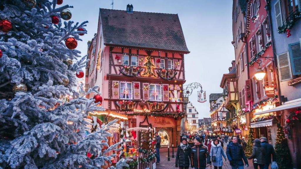 un albero di Natale e gente che cammina per una strada davanti agli edifici di Les VENDANGEURS a Niedermorschwihr