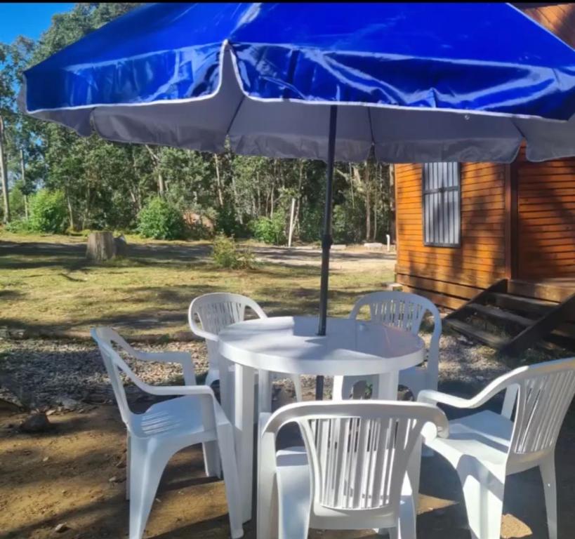 una mesa blanca y sillas con sombrilla azul en Cabaña La Mañana Siguiente, en La Pedrera