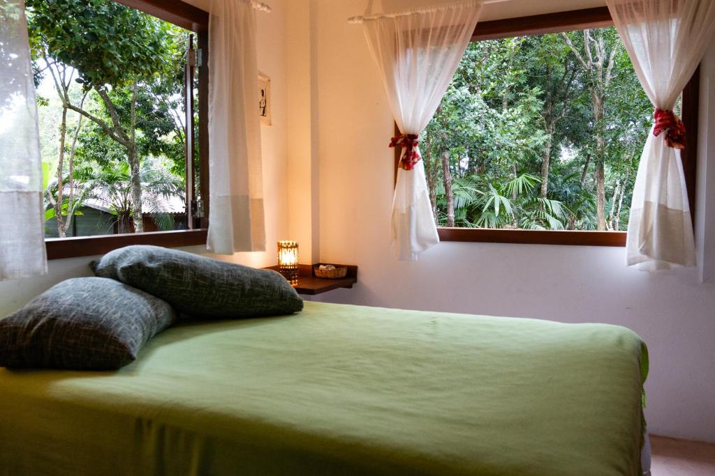 um quarto com uma cama com duas almofadas e duas janelas em Cabana na árvore na Bahia! Para viver uma experiência de hospedagem pertinho da praia em Maraú