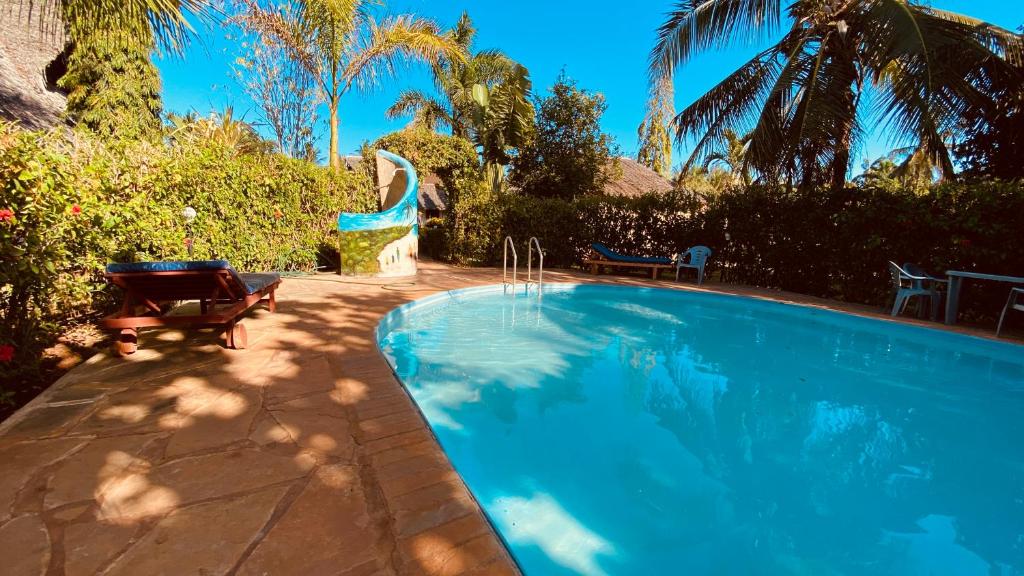 a swimming pool in a yard with two chairs and trees at Villas Dora and Holly in Diani Beach