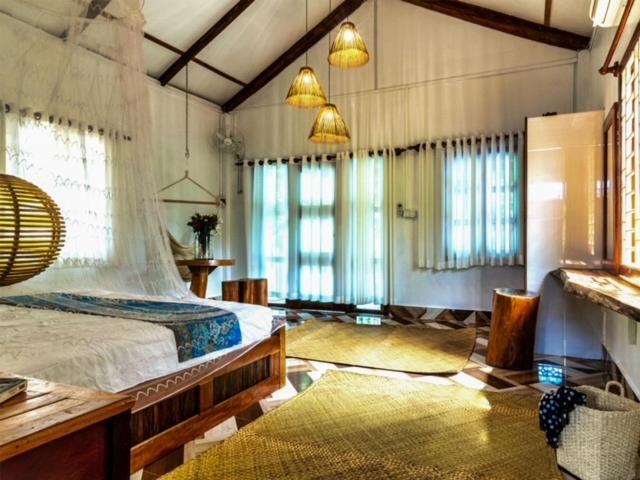 a bedroom with a large bed in a room with windows at Kraoul Seh - Horse Riding Cambodia in Kampot