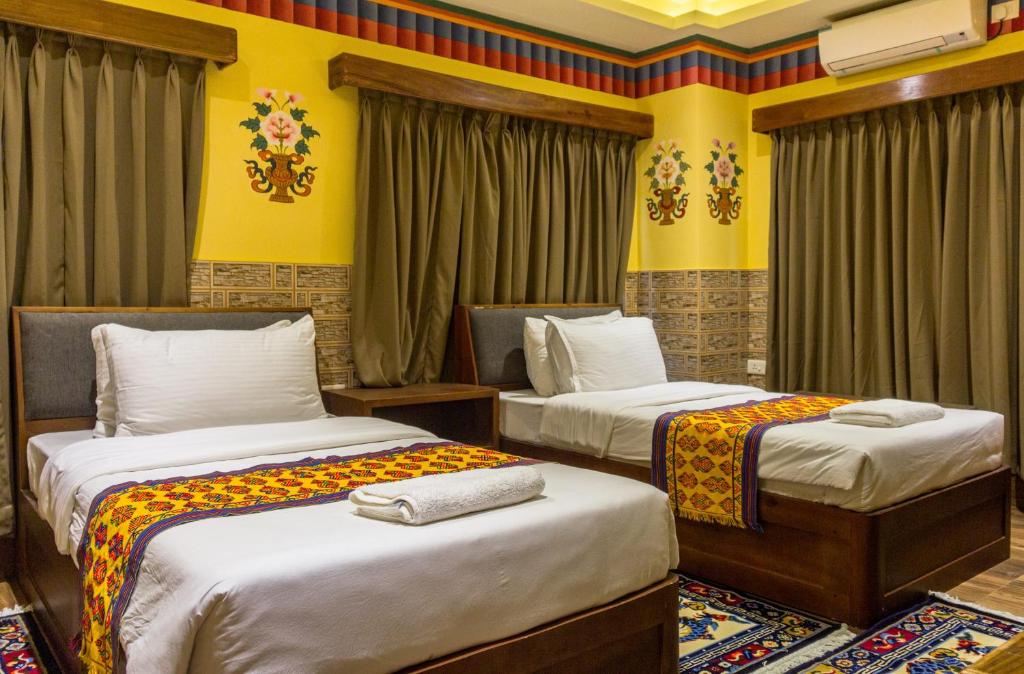 2 Betten in einem Zimmer mit gelben Wänden und Vorhängen in der Unterkunft White Dragon Hotel in Punākha