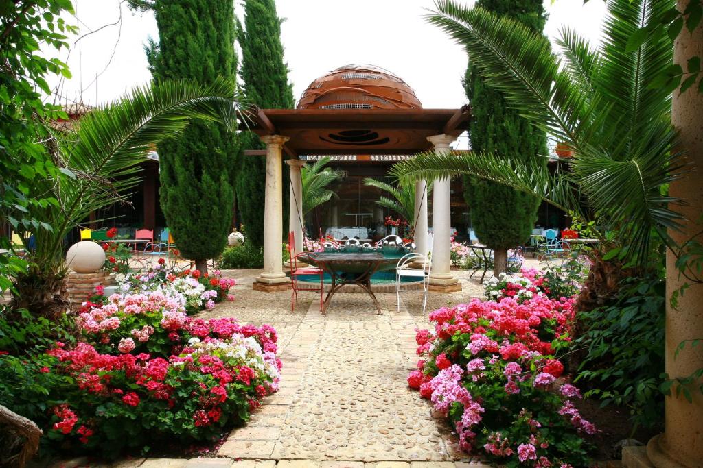 Hotel Boutique Palacio de la Serna في Ballesteros de Calatrava: حديقة فيها ورد وطاولة وكراسي