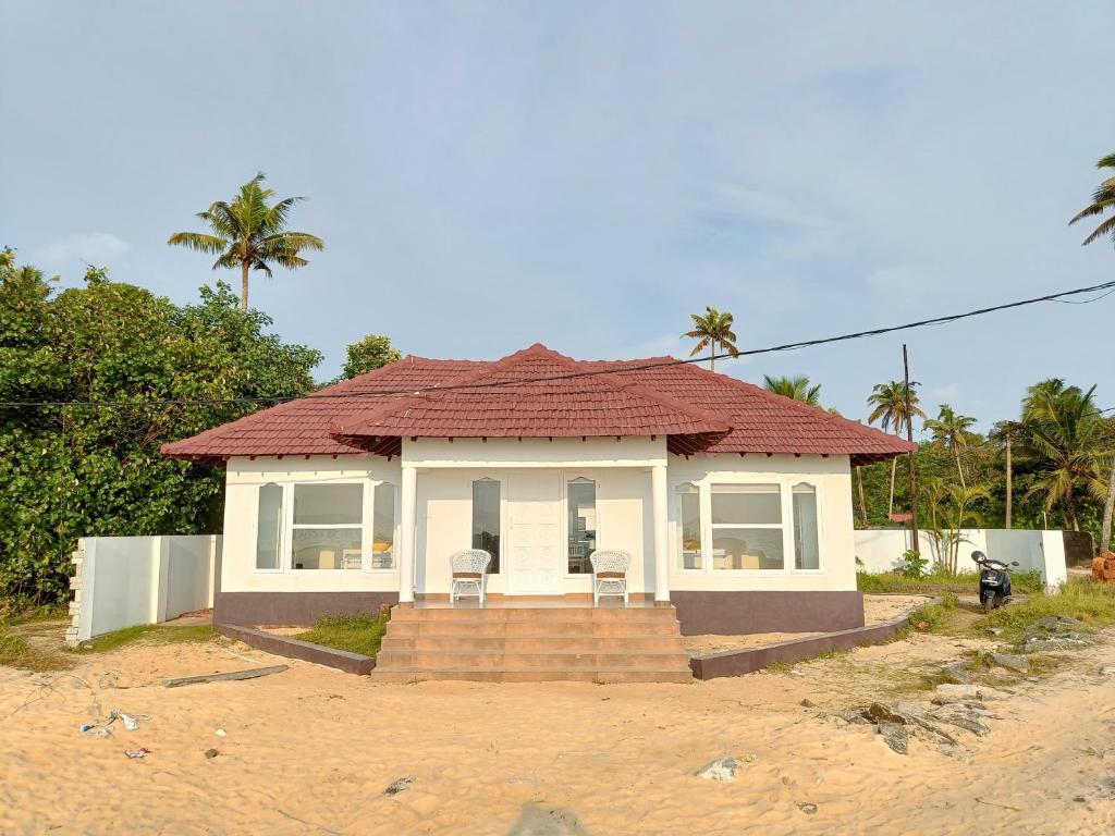 une petite maison avec un toit rouge sur la plage dans l'établissement Seclude Kerala, Beach House, à Mararikulam