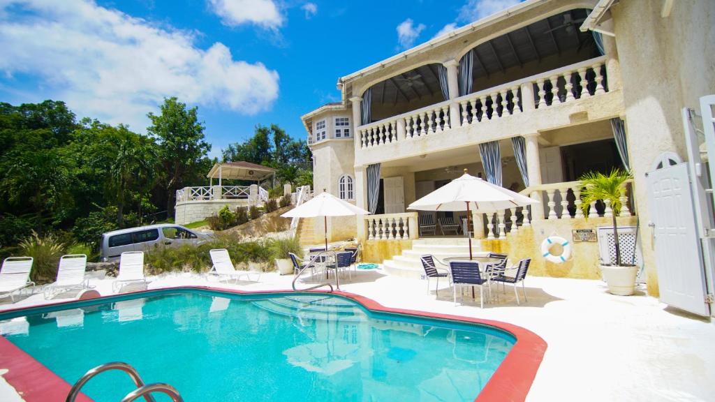 a pool in front of a house with chairs and umbrellas at Sea Symphony Villa in Saint Lucy