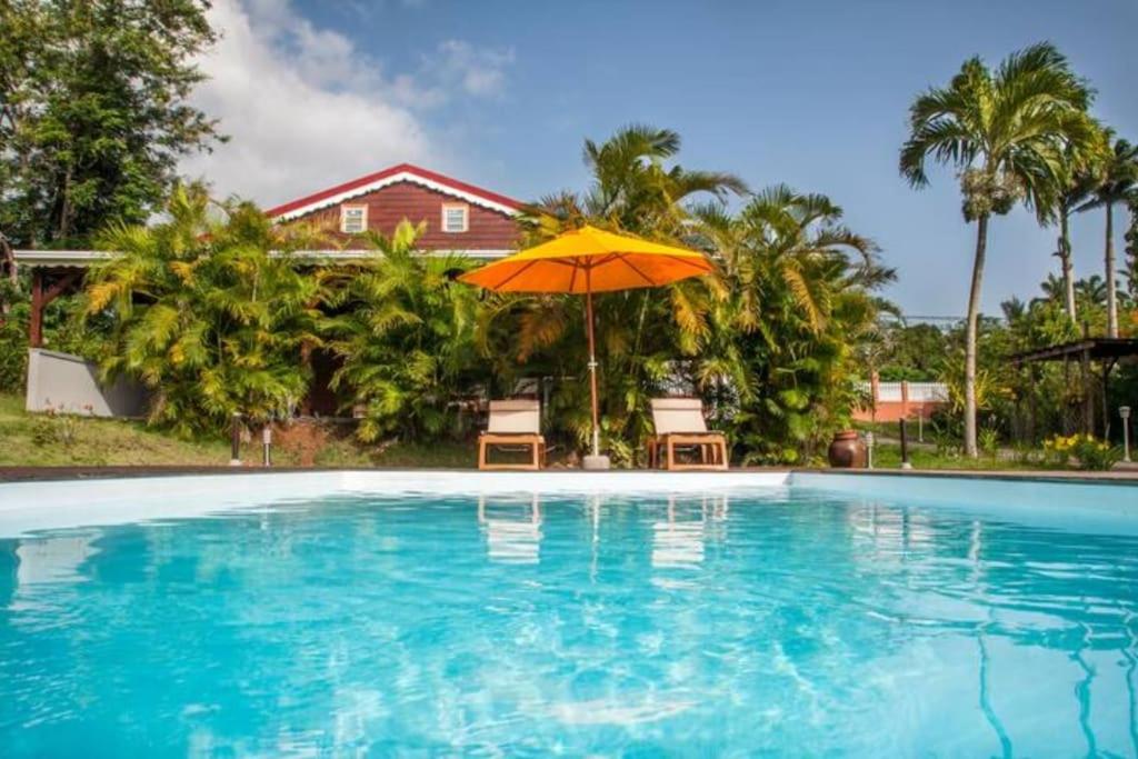 uma piscina com guarda-sol e cadeiras e uma casa em Villa Kylise em Baie-Mahault