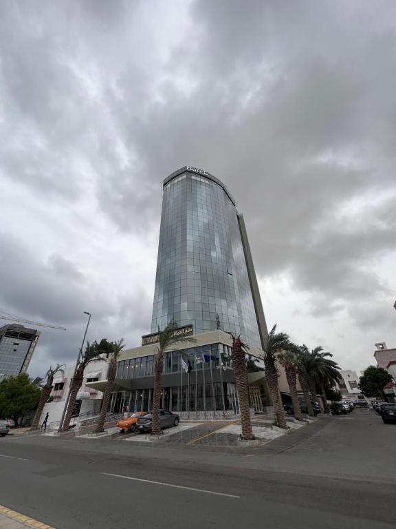 un edificio de cristal alto con palmeras delante en فندق النجم الأزرق - Blue star hotel en Yeda