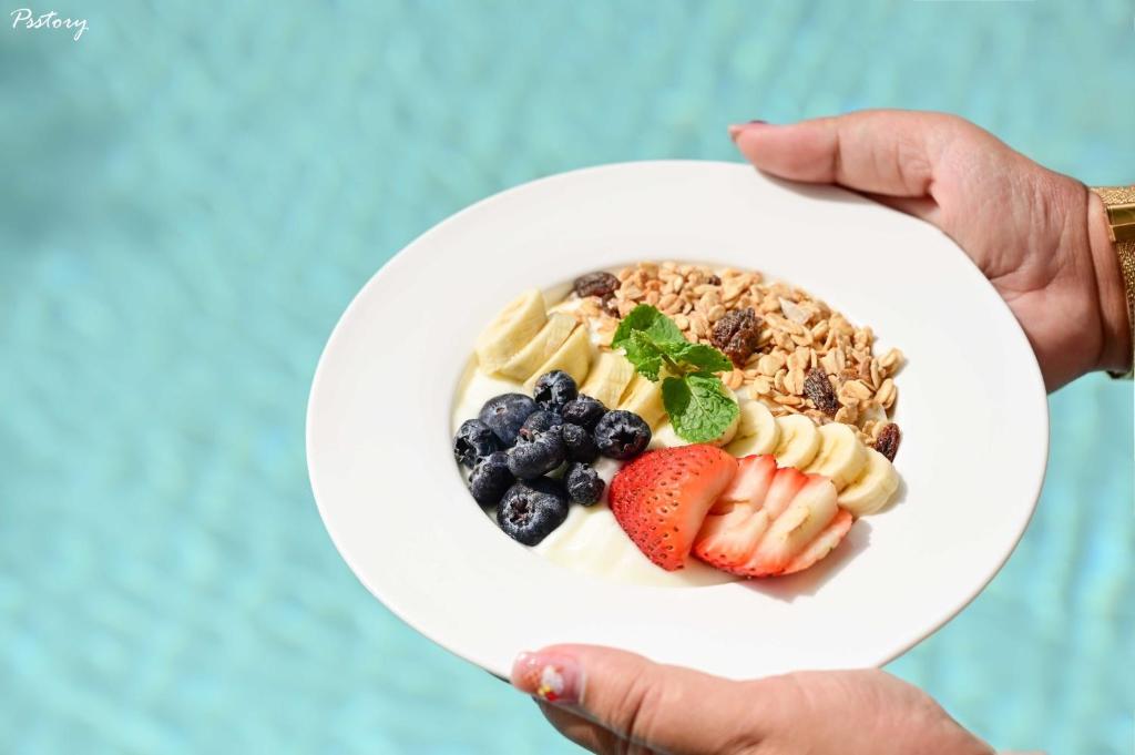 A bowl of yogurt, granola and fresh fruit is held over a blue pool-like background.