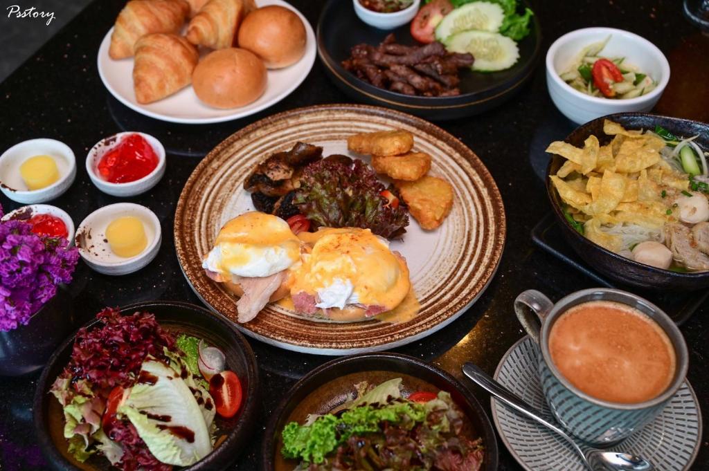 A generously styled breakfast spread with pastries, eggs, meats, salads and hot drinks.