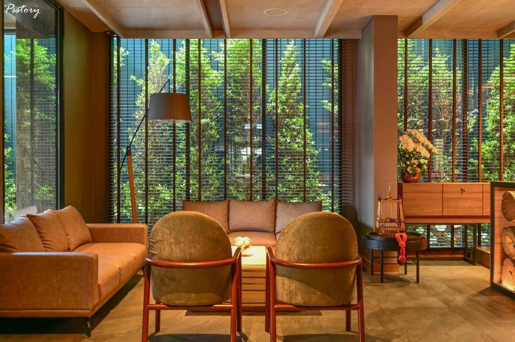 A warm lounge with sofas, armchairs and full-height screened windows overlooking greenery.