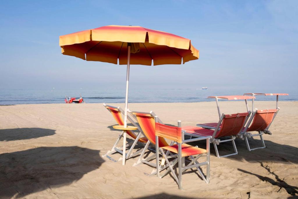 three chairs and an umbrella on the beach at Elena House Apartments in Viareggio