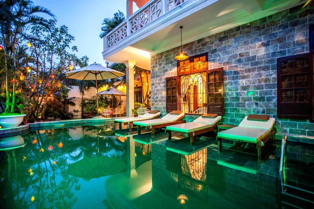 a house with a swimming pool with chairs and an umbrella at Ngan Phu Villa in Hoi An
